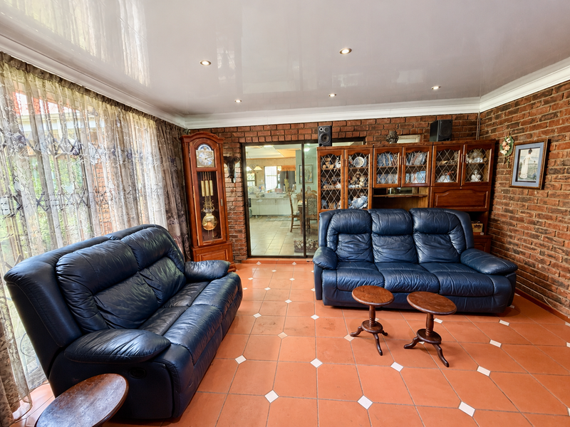 Spacious living room featuring exposed brick walls, terracotta tiled flooring, recessed lighting, and a sliding glass door leading to the adjacent dining area.