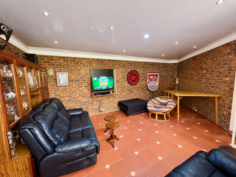 A spacious living room featuring exposed brick walls, tiled flooring, and recessed downlighting, offering a rustic aesthetic with potential for modern updates.
