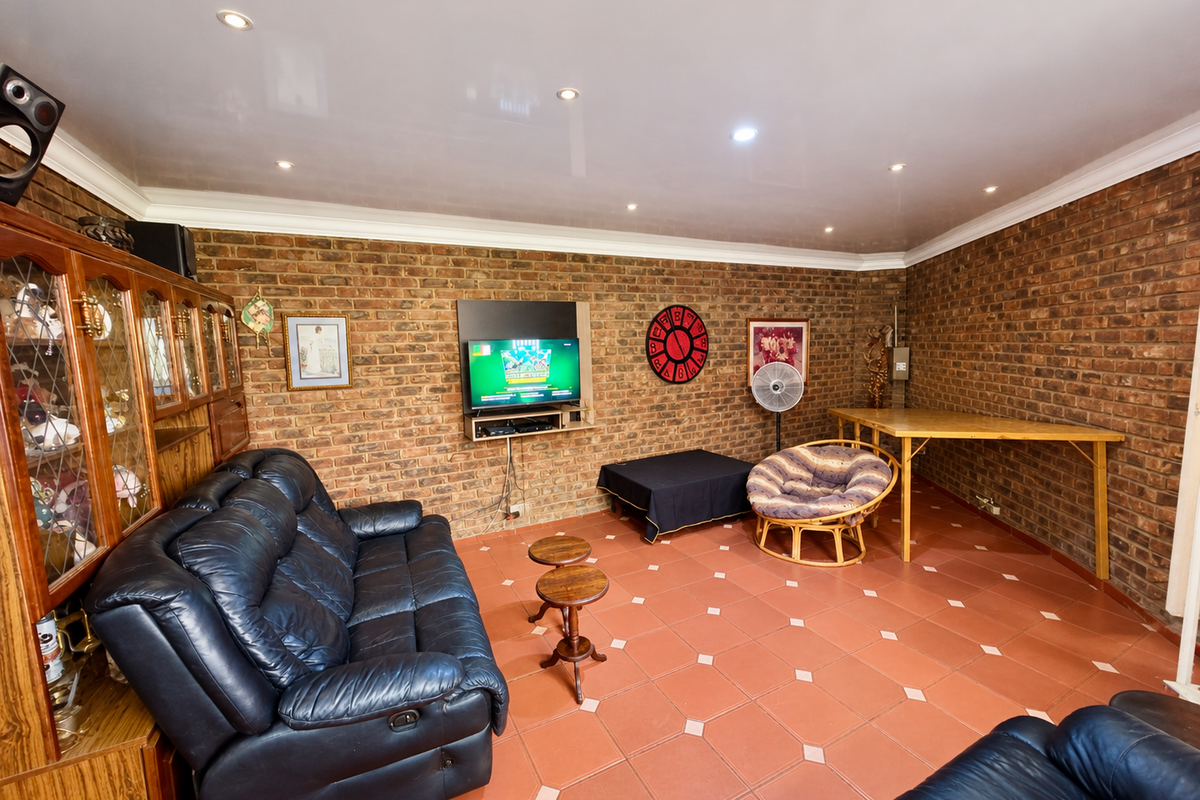 A spacious living room featuring exposed brick walls, tiled flooring, and recessed downlighting, offering a rustic aesthetic with potential for modern updates.