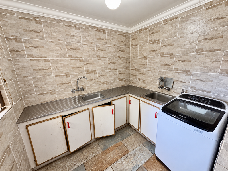 Functional laundry room featuring tiled walls, stainless steel sink, and built-in cabinetry with space for a washing machine.