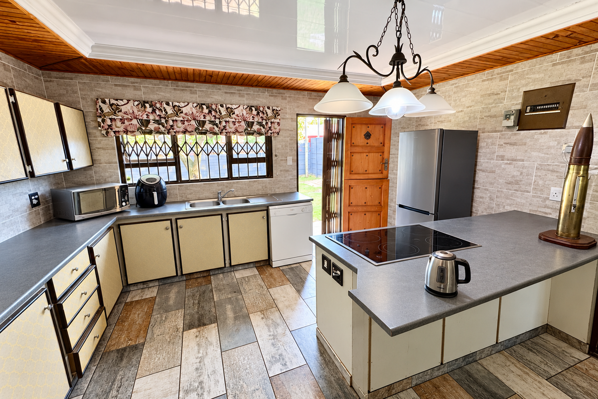 A functional kitchen featuring built-in cabinetry, a central island with an electric hob, double sink, and durable tiled flooring with direct outdoor access.