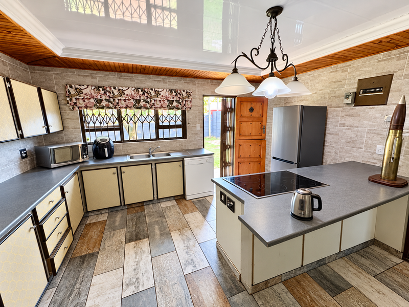 A functional kitchen featuring built-in cabinetry, a central island with an electric hob, double sink, and durable tiled flooring with direct outdoor access.