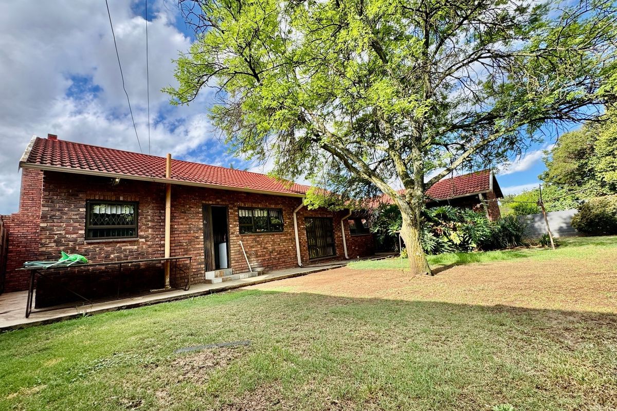 Rear view of a face brick house featuring a tiled roof, security window bars, and a spacious garden area with a large mature tree.