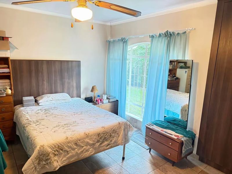 A bedroom featuring tiled flooring, a ceiling fan, and an arched window with security bars, complemented by a built-in wardrobe.