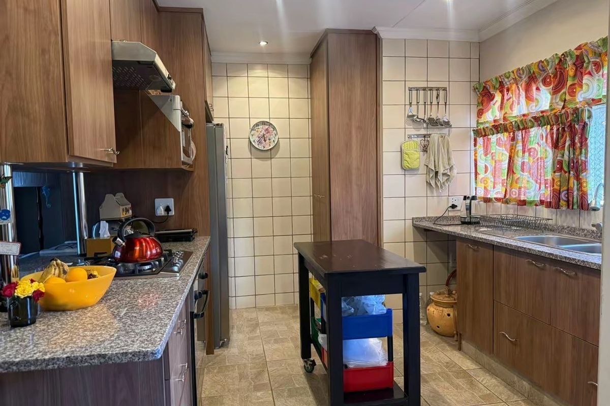 Functional kitchen featuring wood-look laminate cabinetry, granite countertops, a gas hob with extractor fan, and tiled backsplash with ample storage space.