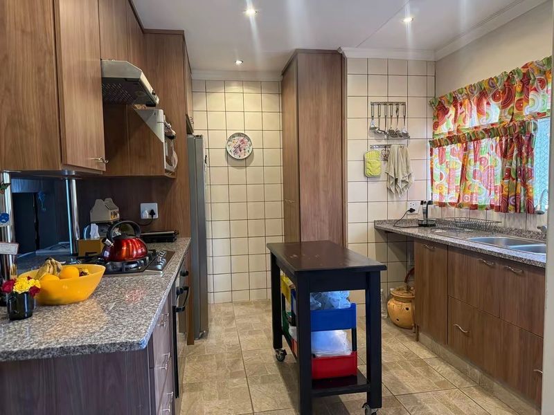 Functional kitchen featuring wood-look laminate cabinetry, granite countertops, a gas hob with extractor fan, and tiled backsplash with ample storage space.