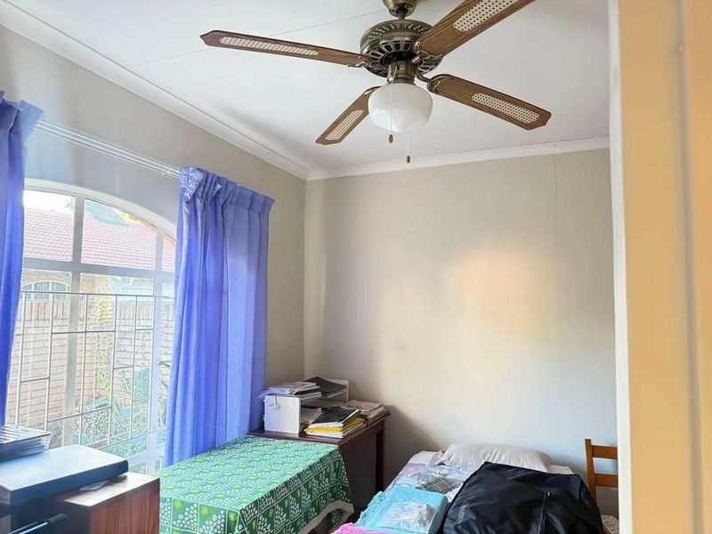 A functional bedroom featuring a ceiling fan and an arched window with security bars, offering natural light and ventilation.