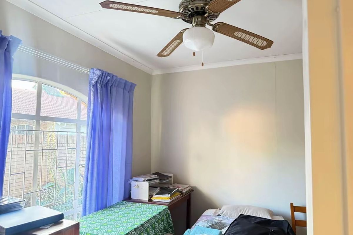 A functional bedroom featuring a ceiling fan and an arched window with security bars, offering natural light and ventilation.