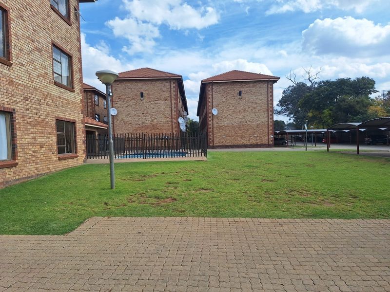 Exterior view of an apartment complex featuring face brick buildings, a communal lawn area, paved pathways, and covered parking bays.