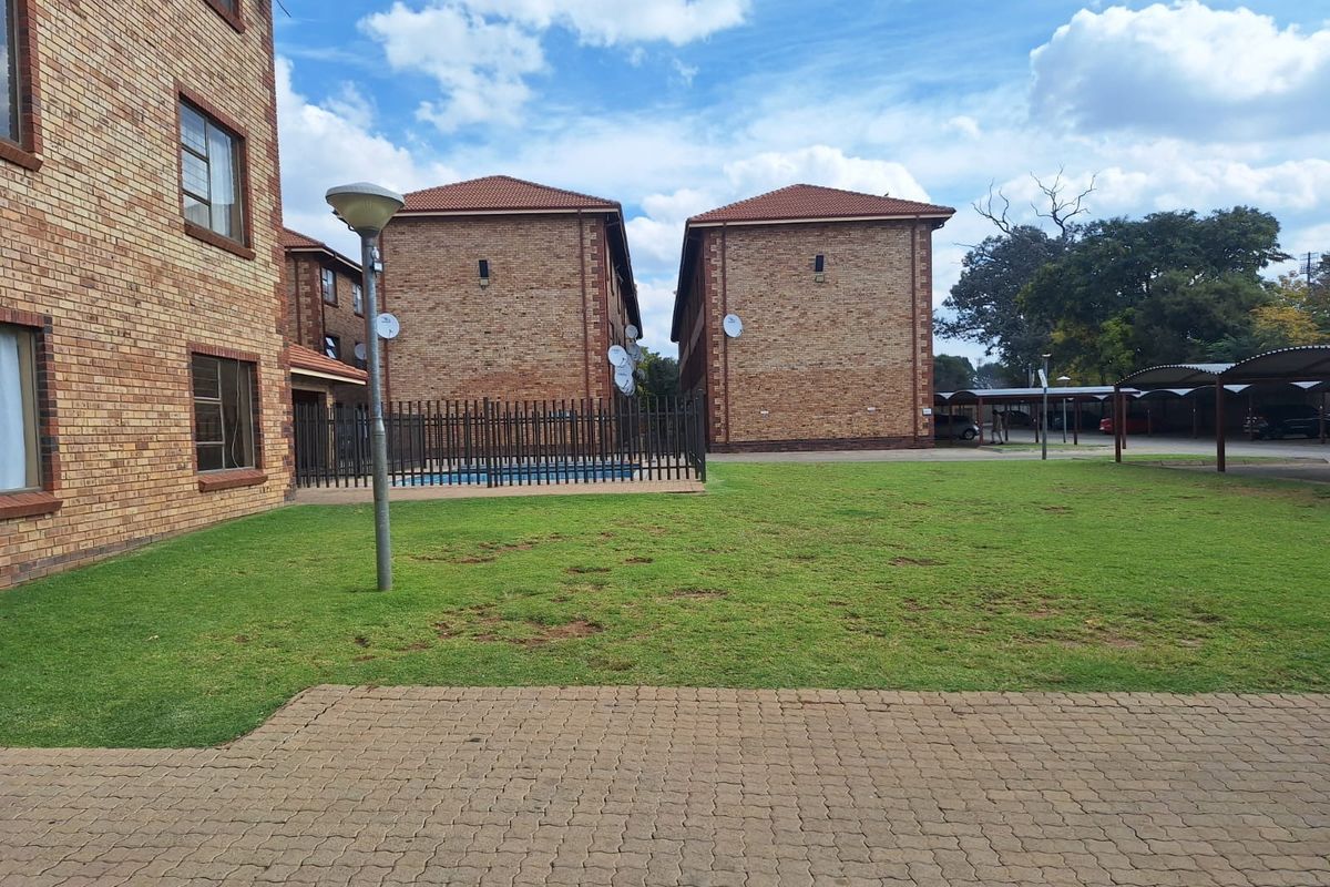 Exterior view of an apartment complex featuring face brick buildings, a communal lawn area, paved pathways, and covered parking bays.