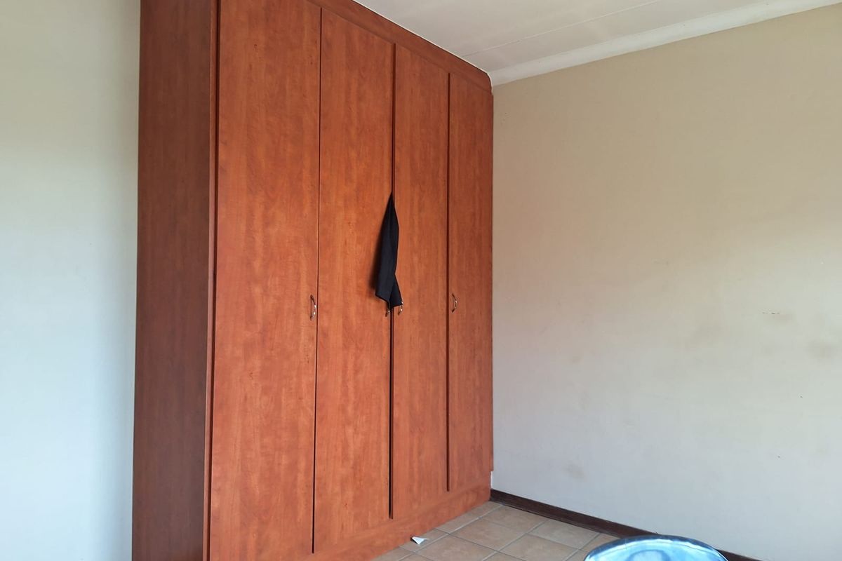 A bedroom featuring a large built-in wooden wardrobe and tiled flooring, offering a functional space ready for personalization.
