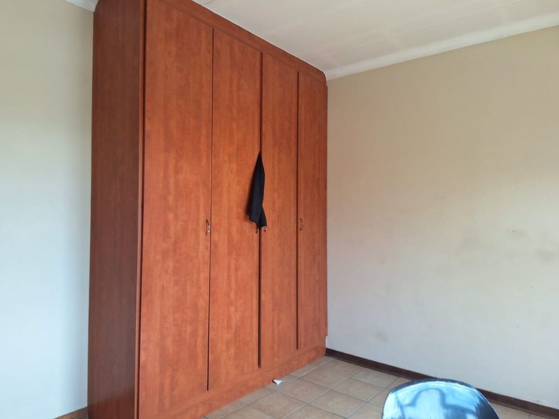 A bedroom featuring a large built-in wooden wardrobe and tiled flooring, offering a functional space ready for personalization.