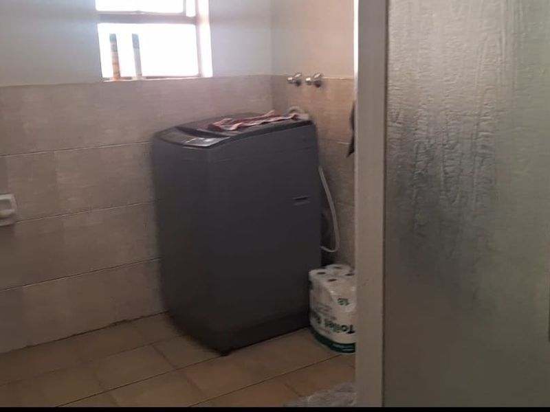 A functional laundry area featuring tiled walls and flooring, equipped with necessary plumbing connections for a washing machine.