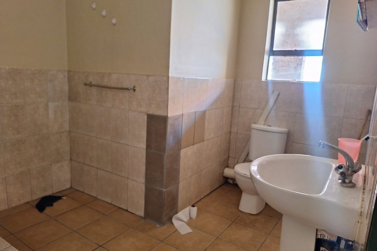 A functional bathroom featuring a pedestal basin, toilet, and tiled finishes. The space requires cosmetic updates and repairs to the wall tiling and plumbing.