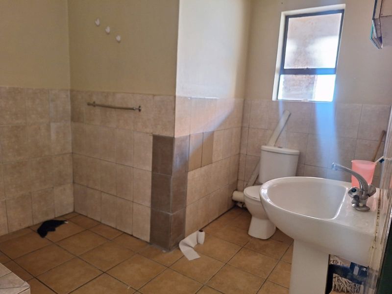 A functional bathroom featuring a pedestal basin, toilet, and tiled finishes. The space requires cosmetic updates and repairs to the wall tiling and plumbing.