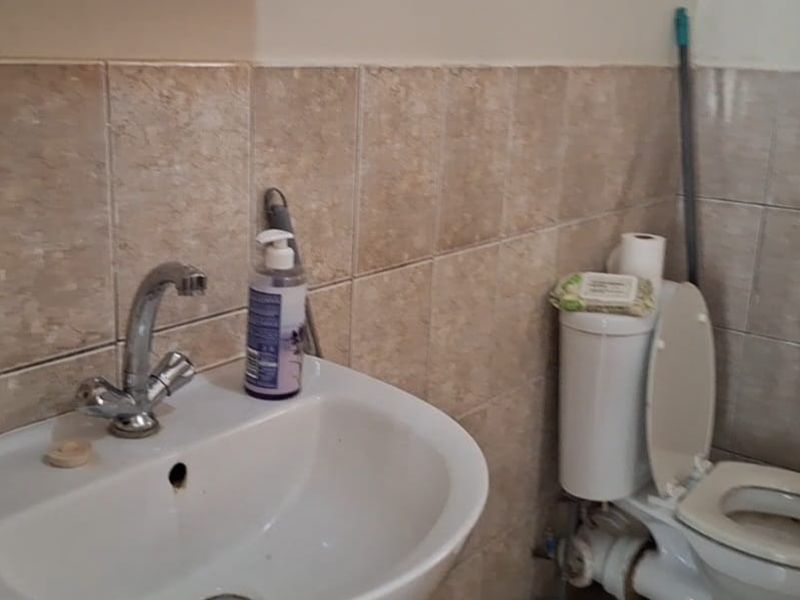 A functional bathroom featuring a pedestal basin with chrome faucet and a standard toilet, finished with neutral ceramic wall tiling.