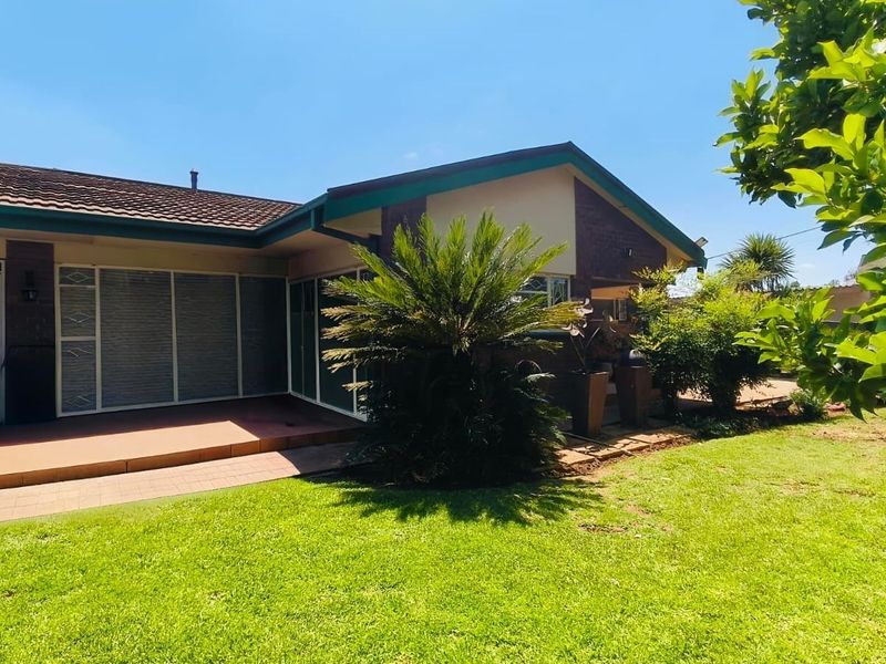 Front elevation of a single-story brick house featuring a tiled roof, paved patio area, and secure entrance with a metal security gate.