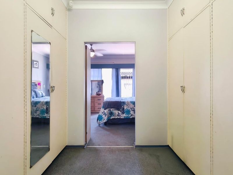 A hallway featuring extensive built-in floor-to-ceiling cupboards with a full-length mirror, providing ample storage space and leading into an adjacent bedroom.
