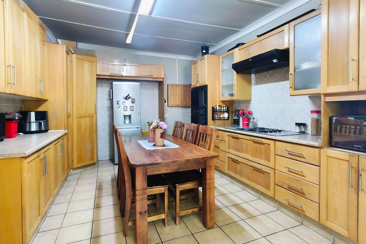 Spacious kitchen featuring extensive wooden cabinetry, tiled flooring, built-in oven, and a central dining area, offering a functional layout with classic finishes.