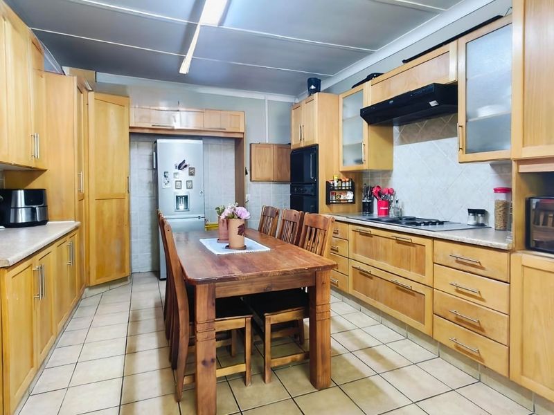 Spacious kitchen featuring extensive wooden cabinetry, tiled flooring, built-in oven, and a central dining area, offering a functional layout with classic finishes.