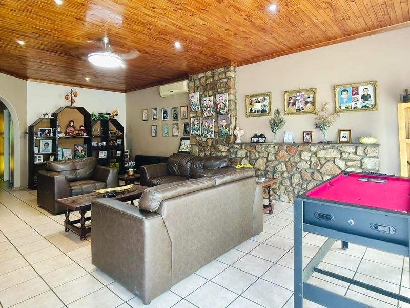 Spacious living room featuring a prominent stone feature wall, warm timber ceiling, and neutral tiled flooring, offering a comfortable and character-filled family space.