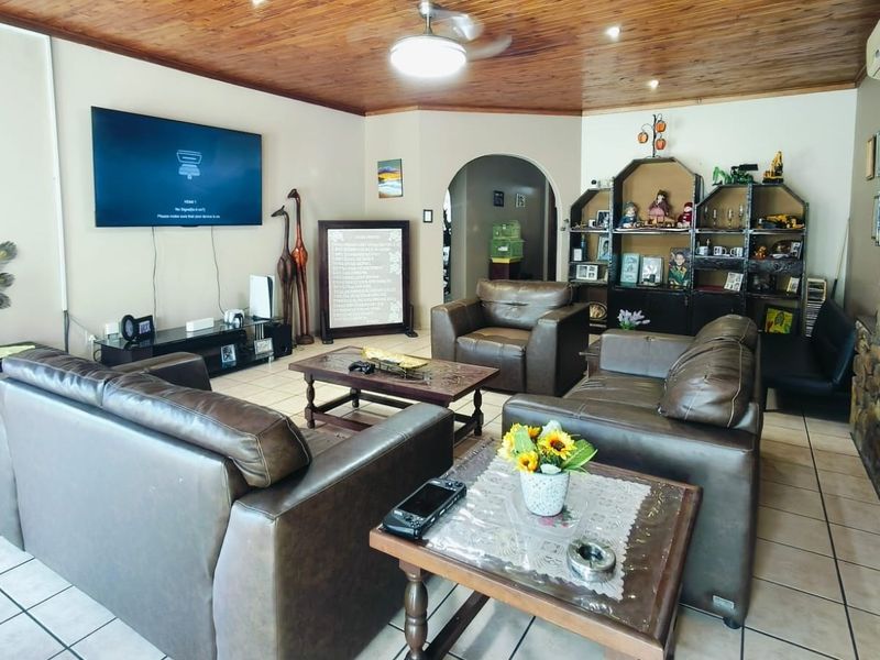 Spacious living room featuring a warm timber tongue and groove ceiling, ceramic tiled flooring, and a rustic stone feature wall.