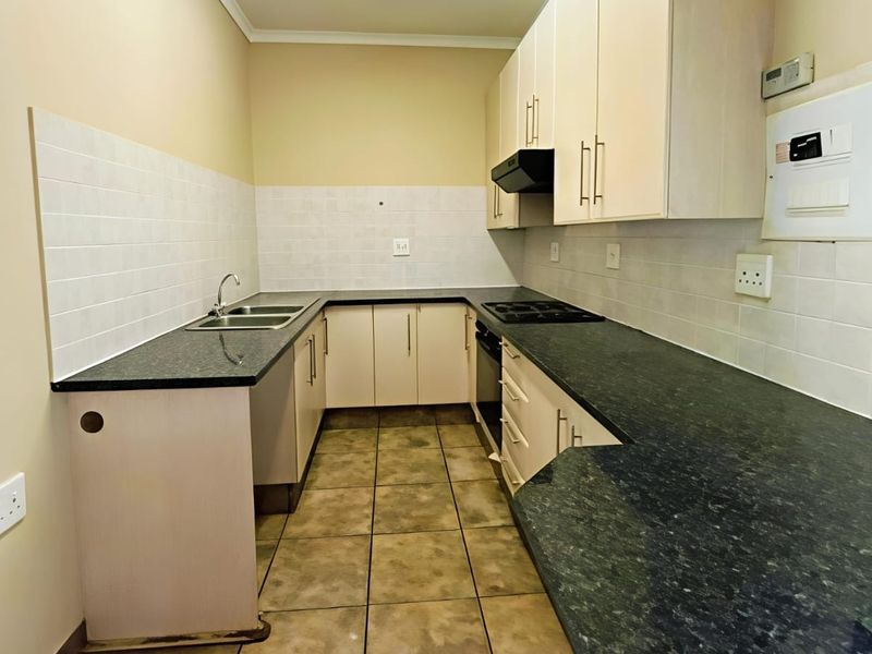 A functional, empty kitchen featuring built-in cabinetry, dark laminate countertops, a built-in oven with hob, and tiled flooring throughout.