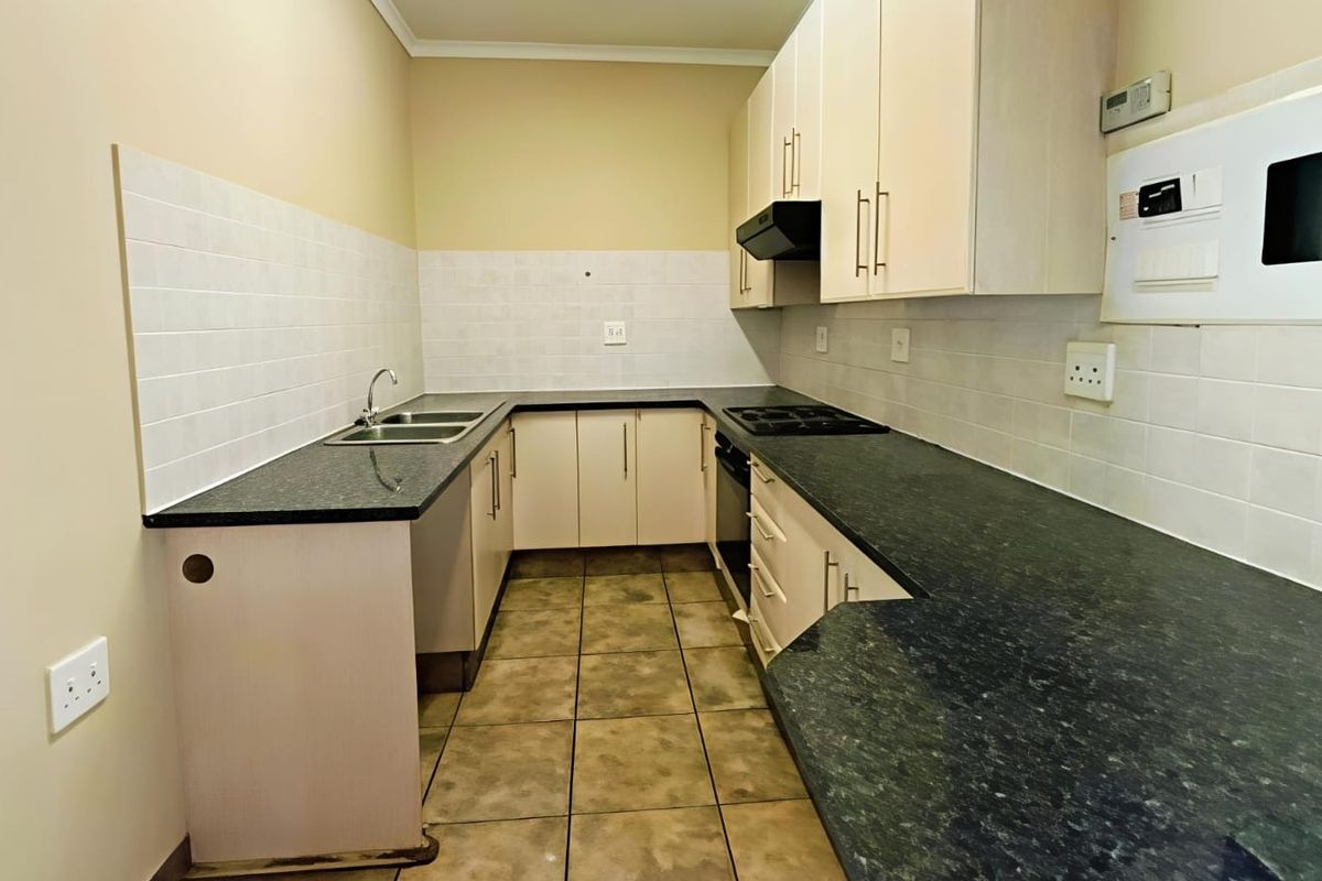 A functional, empty kitchen featuring built-in cabinetry, dark laminate countertops, a built-in oven with hob, and tiled flooring throughout.