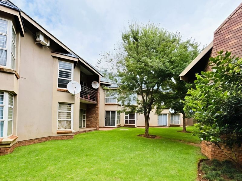 A view of the rear exterior of the apartment complex, featuring a shared garden area, brick facade, and balcony access.