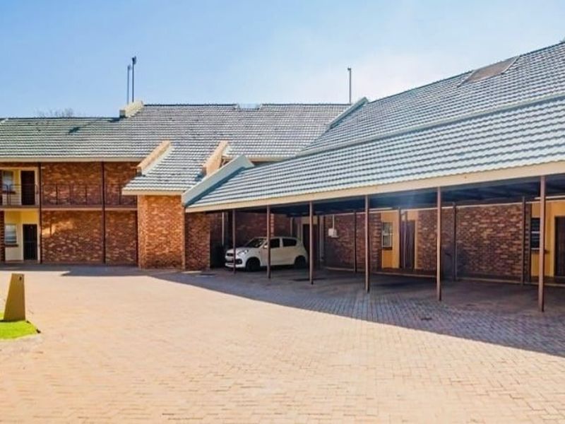 Exterior view of an apartment complex featuring a brick facade, tiled roof, and a covered parking area with a paved driveway.