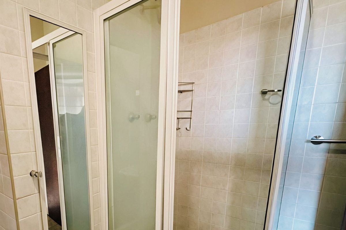 A functional bathroom featuring a tiled shower enclosure with a frosted glass door and a wall-mounted towel rail.