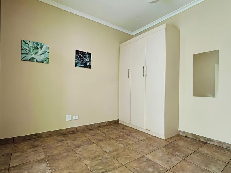 A clean, empty bedroom featuring neutral walls, tiled flooring, and a functional built-in wardrobe with ample storage space.