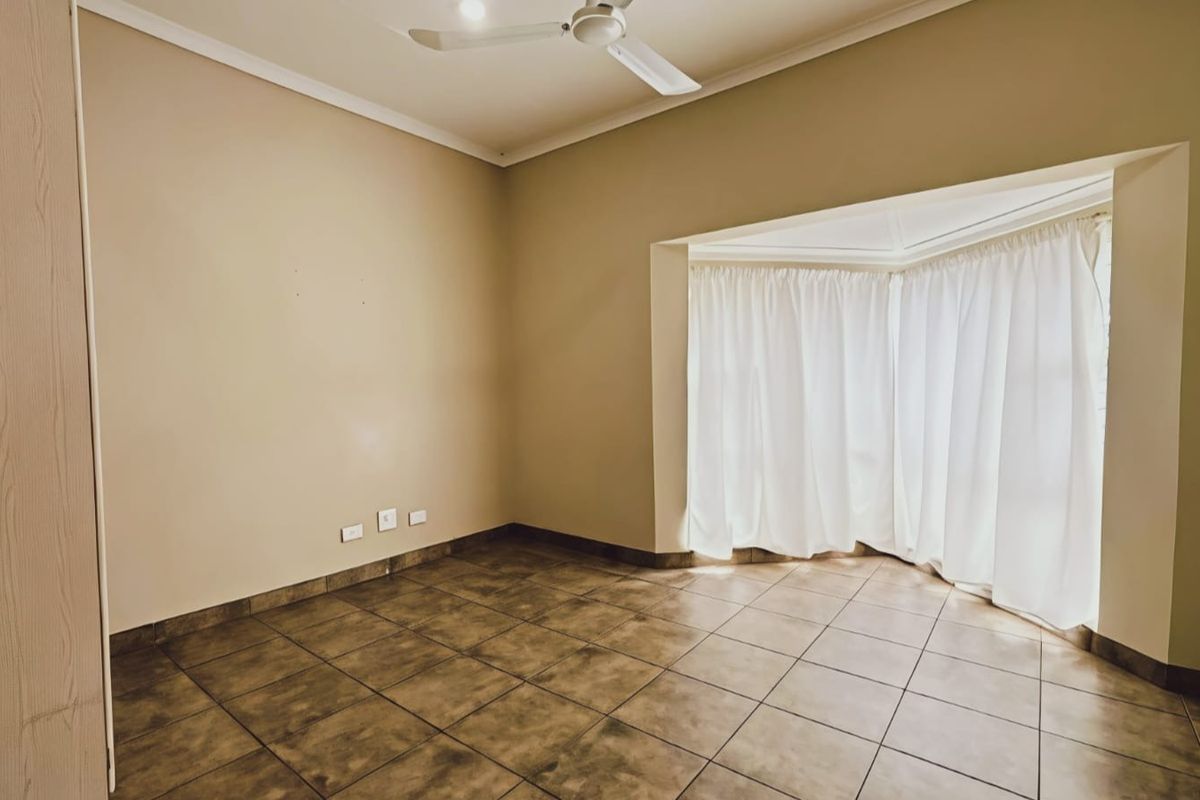 An empty bedroom featuring tiled flooring, a ceiling fan, and a large bay window with curtains.