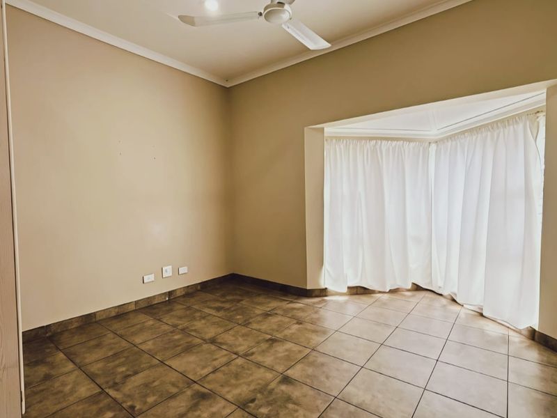 An empty bedroom featuring tiled flooring, a ceiling fan, and a large bay window with curtains.