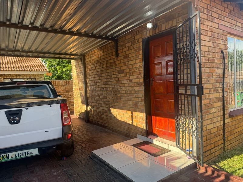 Front entrance area featuring a covered carport, brick facade, and a secure entrance door with a metal security gate.