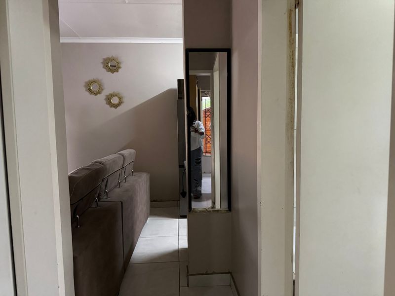 A view through a hallway featuring tiled flooring and coving, showing signs of wear on the door frame and skirting.