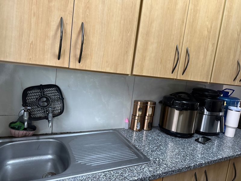 A functional kitchen area featuring light wood-tone cabinetry, a granite countertop, and a stainless steel sink with a tiled backsplash.