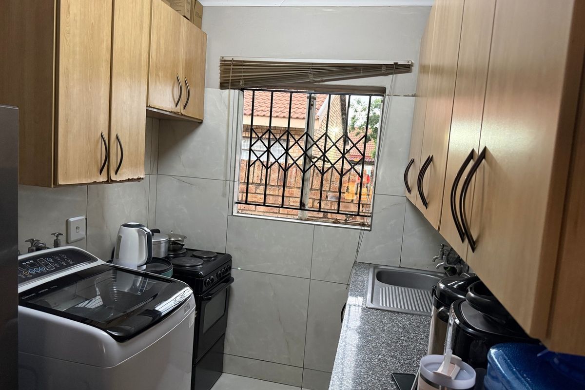 Compact kitchen featuring laminate cabinetry, granite countertops, stainless steel sink, and tiled backsplash with a security-fitted window.