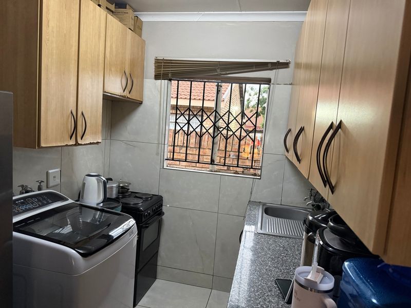 Compact kitchen featuring laminate cabinetry, granite countertops, stainless steel sink, and tiled backsplash with a security-fitted window.