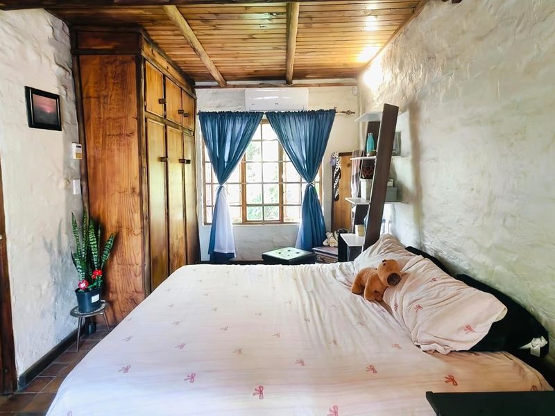 A rustic bedroom featuring textured stone walls, a timber-paneled ceiling, built-in wooden cabinetry, and an integrated air conditioning unit.