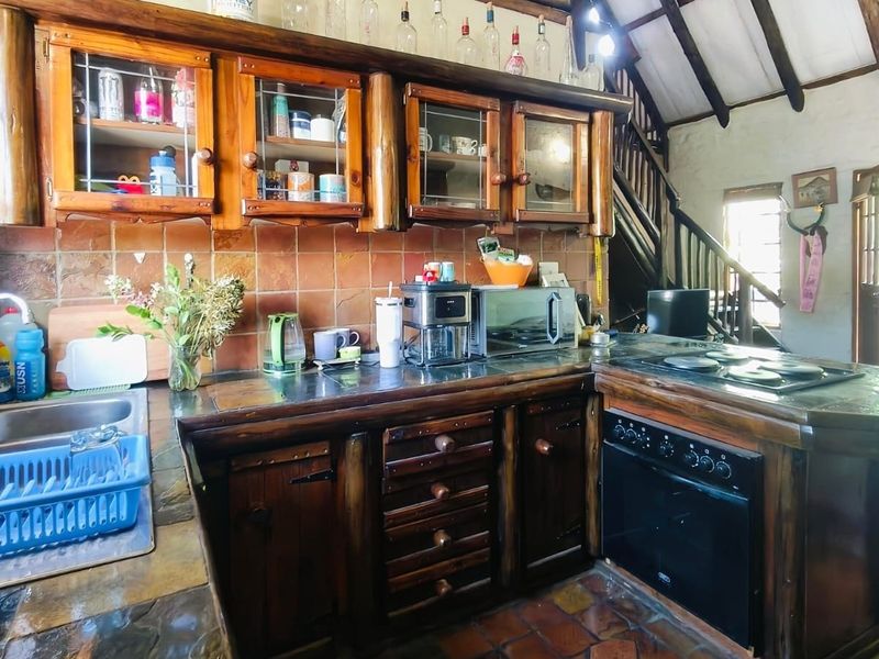 Rustic kitchen featuring dark wood cabinetry, stone countertops, integrated oven and hob, and exposed timber ceiling beams with terracotta flooring.