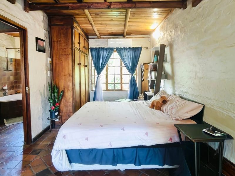 Rustic bedroom featuring textured stone walls, exposed timber ceiling beams, terracotta tiled flooring, and a built-in wooden wardrobe with an adjoining bathroom.