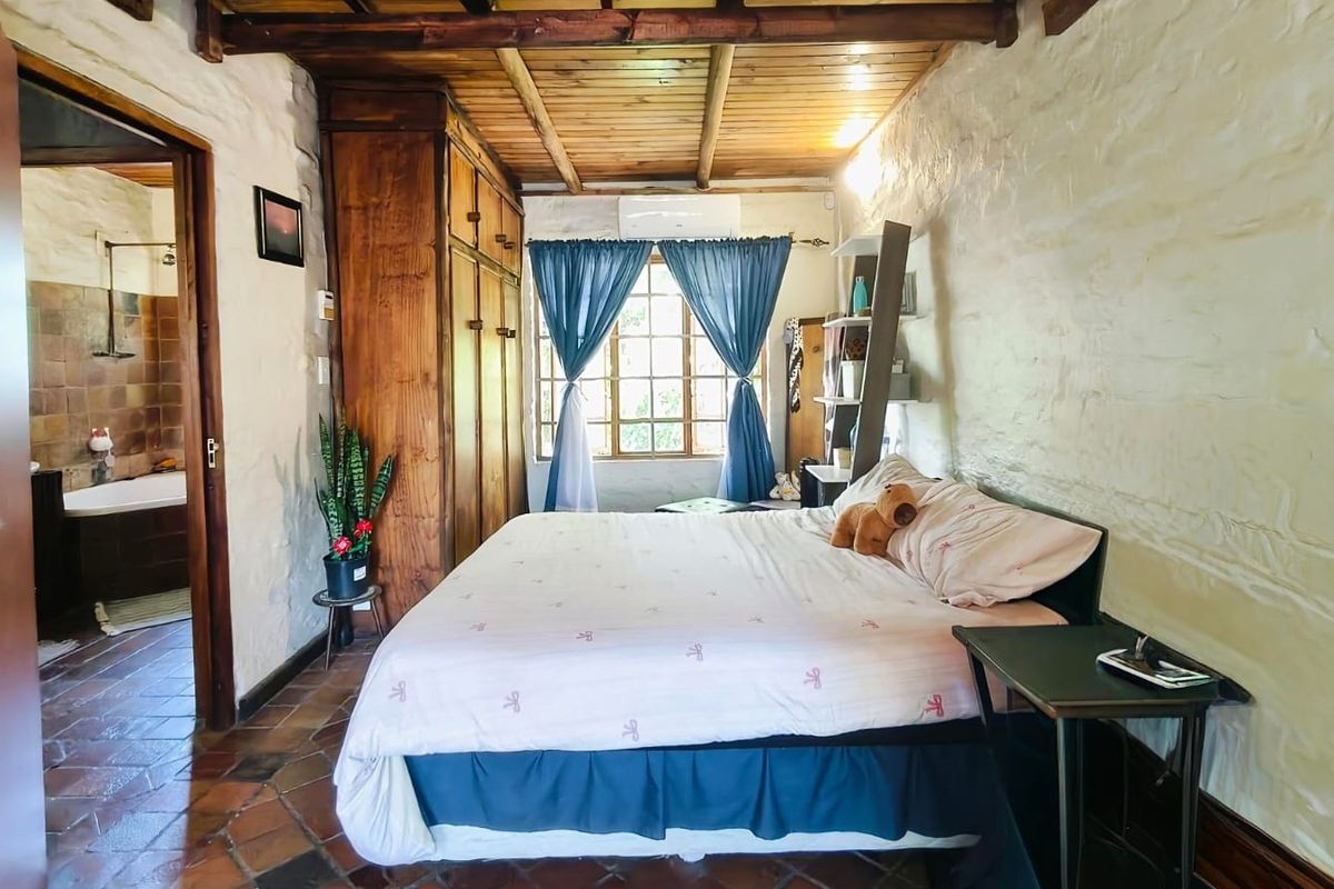 Rustic bedroom featuring textured stone walls, exposed timber ceiling beams, terracotta tiled flooring, and a built-in wooden wardrobe with an adjoining bathroom.