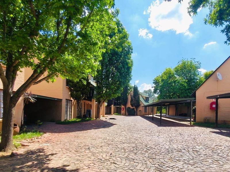 A well-maintained apartment complex exterior featuring a cobblestone driveway, covered parking carports, and established landscaping.