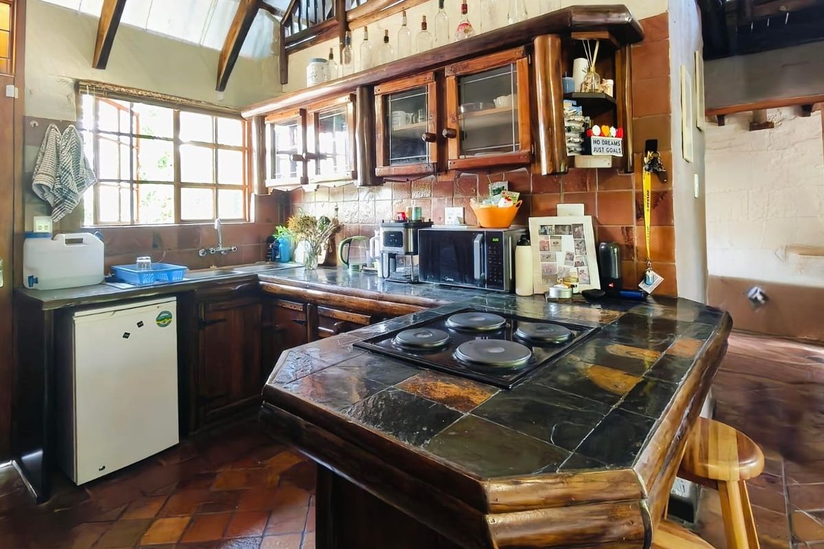 Rustic kitchen featuring dark wood cabinetry, slate tile countertops, an integrated electric hob, and exposed timber ceiling beams with terracotta flooring.