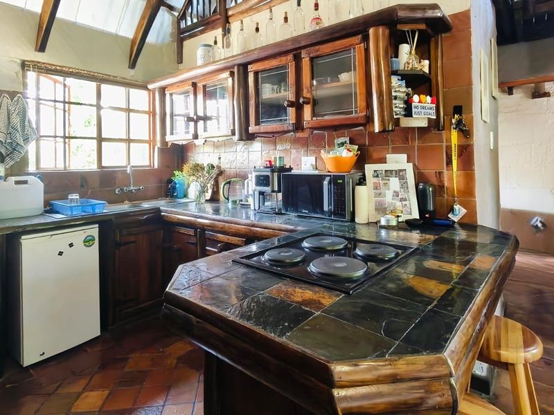 Rustic kitchen featuring dark wood cabinetry, slate tile countertops, an integrated electric hob, and exposed timber ceiling beams with terracotta flooring.