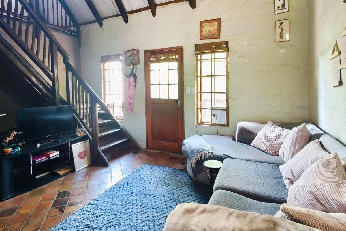 A rustic living room featuring exposed timber ceiling beams, terracotta tiled flooring, and a wooden staircase leading to an upper level.