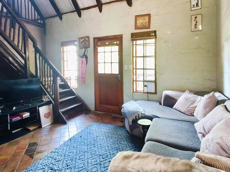 A rustic living room featuring exposed timber ceiling beams, terracotta tiled flooring, and a wooden staircase leading to an upper level.