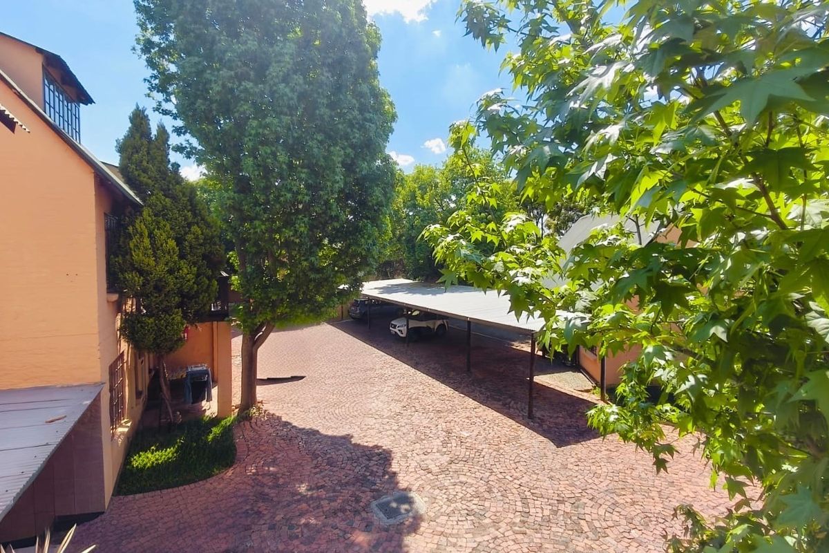 An elevated view of a rear courtyard featuring a cobblestone driveway and a covered carport area surrounded by mature trees.