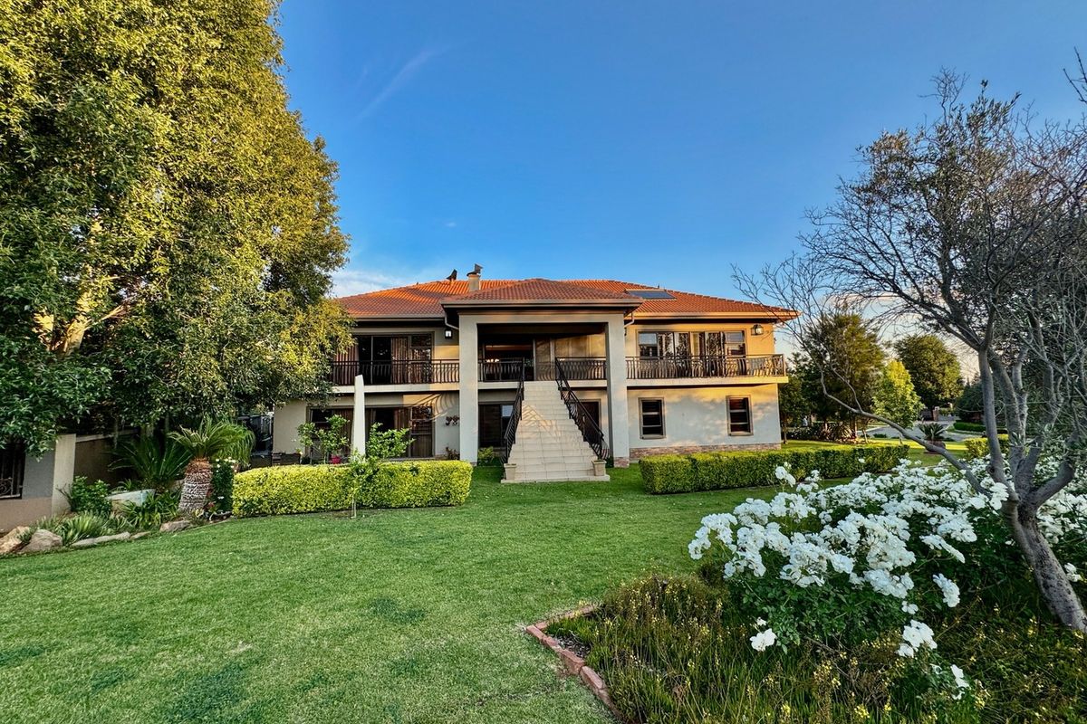 A well-maintained double-story residence featuring a central staircase, expansive upper balcony with wrought iron railings, and a beautifully landscaped rear garden.